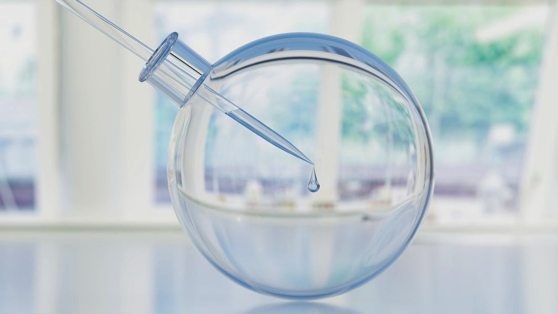Dropper releasing a clear liquid into a transparent round container symbolizing the hydrating benefits of hyaluronic acid for glowing skin