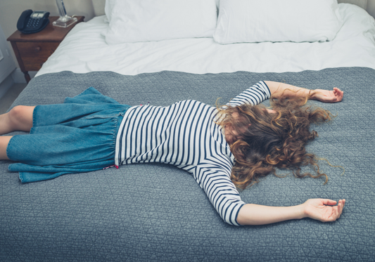 Woman lying face down on bed feeling exhausted, representing fatigue and need for dietary supplements for fatigue relief and energy boost.